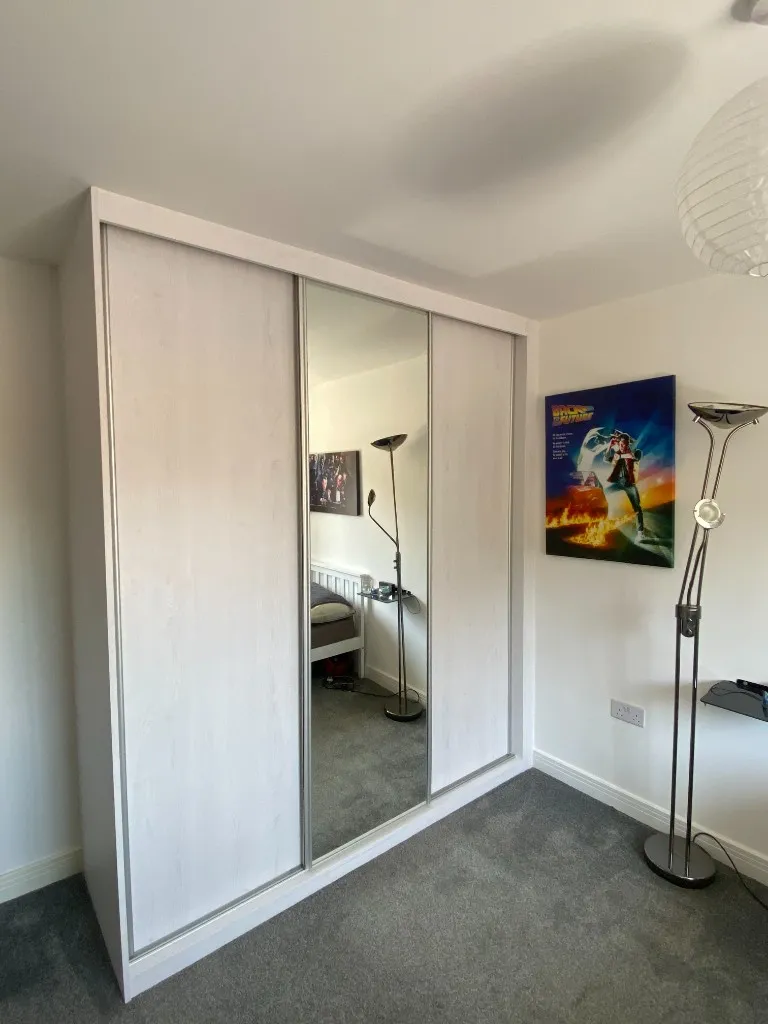Closed white-frame three-door sliding wardrobe with centre mirror